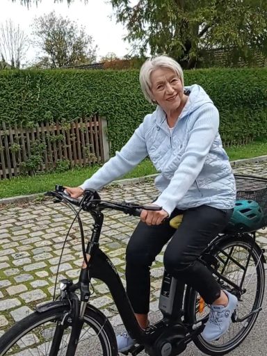 Ältere Frau fährt auf einem Elektro-Fahrrad in einer parkähnlichen Umgebung.