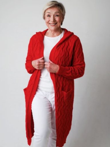 Lächelnde Frau in rotem, gestricktem Mantel mit Taschen und weißem Oberteil.