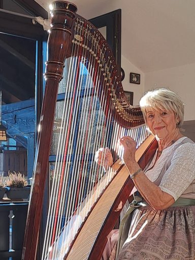 Eine ältere Frau spielt auf einer Harfe in einem hellen Raum.